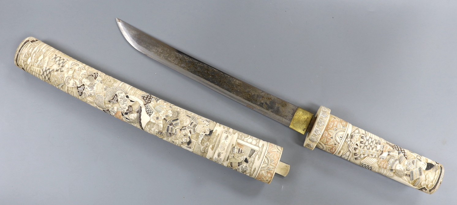 A Japanese carved and coloured ivory tanto, Meiji period, the hilt and scabbard carved to both sides with figures in ceremonial dress, the whole etched in black , green and red, the separate kodzuka with ivory blade and